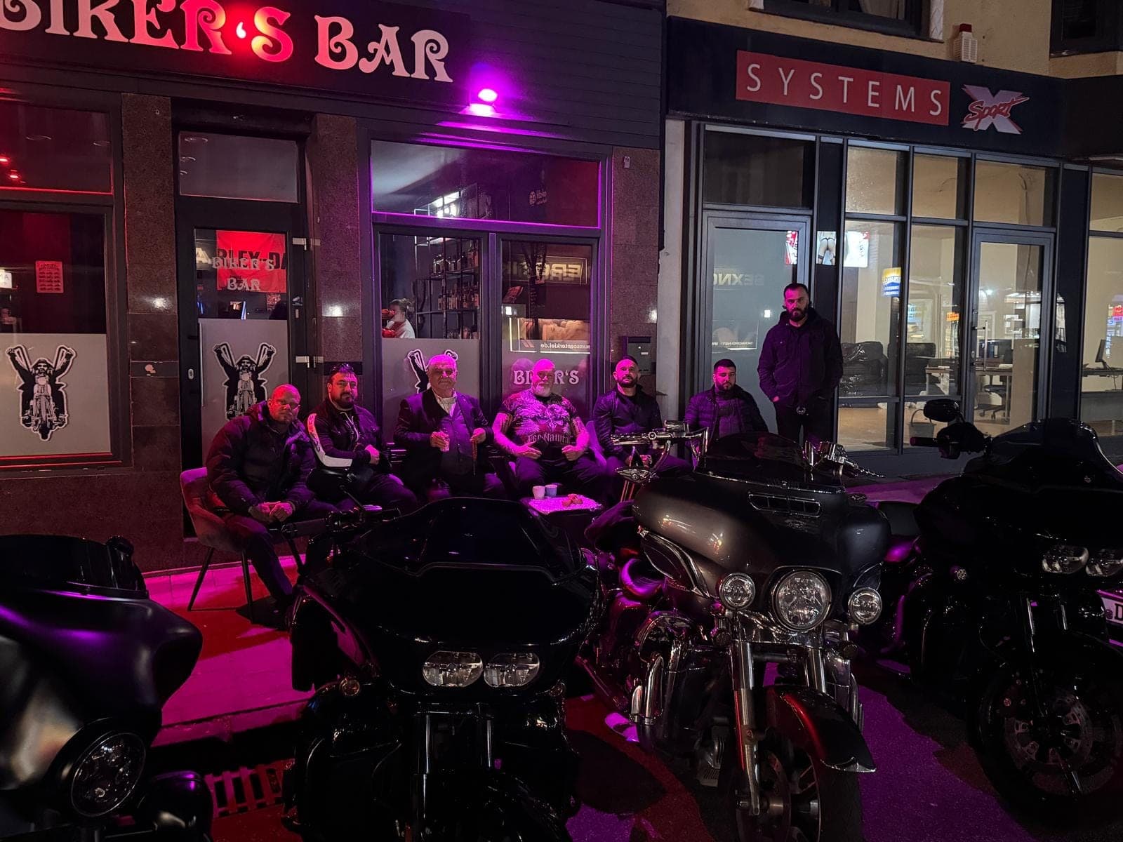 Gäste unter dem Neonschriftzug vor der Bar bei Nacht